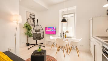 Ein modernes Wohnzimmer mit einer Couch, einem Hängesessel, einem Esstisch mit Stühlen, einem Fernseher und einer Küchenzeile mit Spüle.