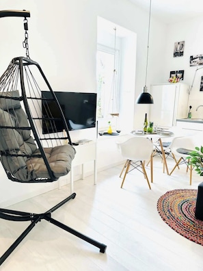 Een moderne woonruimte met een hangstoel, een eethoek met stoelen, een keuken en een televisie.