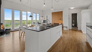 Una cocina moderna con una isla grande, un comedor con sillas y vistas amplias a través de ventanas grandes.