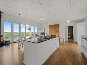 Une cuisine moderne dotée d’un grand îlot central, d’un coin repas avec des chaises et offrant une vue dégagée grâce à de grandes fenêtres.