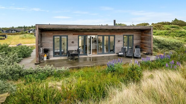 Una casa moderna con terraza, puertas corredizas de vidrio y mobiliario exterior.