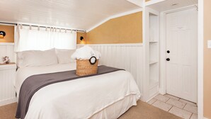 Quarto com cama, um cesto de toalhas, mesa de cabeceira, abajur e porta com a inscrição 'Acesso à Lavanderia'.