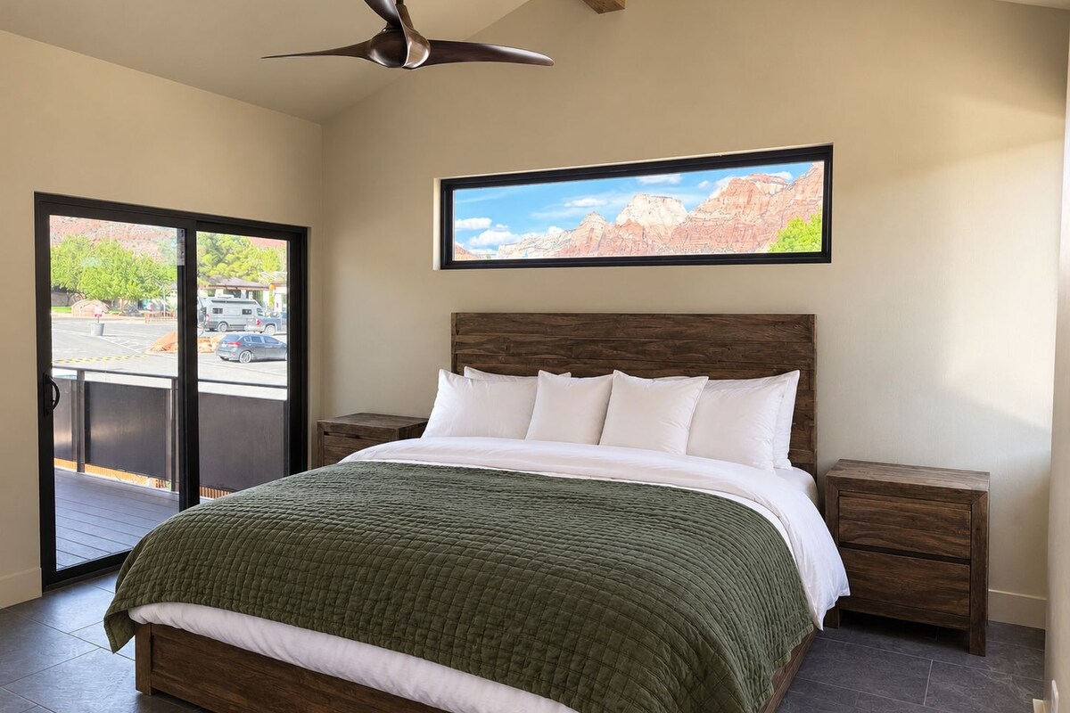 A bedroom with a bed, a nightstand, a wooden headboard, a ceiling fan, and a window with a mountain view.