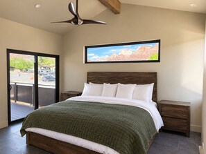 A bedroom with a bed, a nightstand, a wooden headboard, a ceiling fan, and a window with a mountain view. - Purple Sage Place (Springdale)