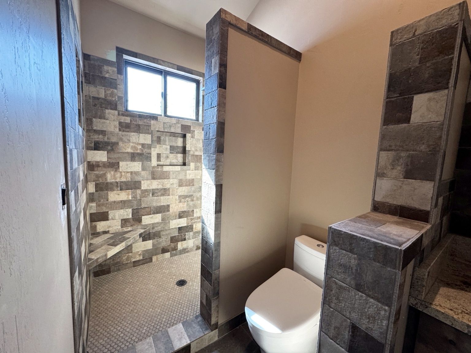 A bathroom with a shower area, a toilet, and a window.