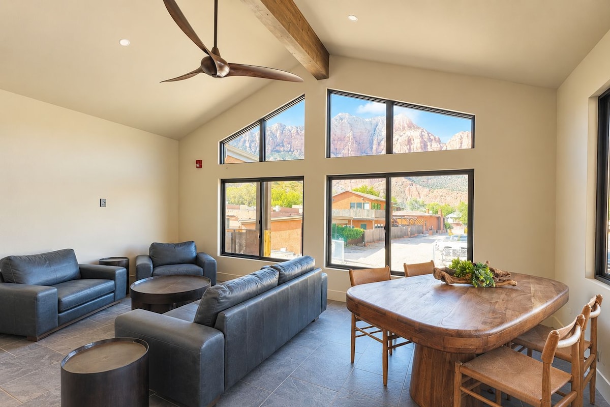 A spacious living area with a large sofa, a dining table with chairs, and a ceiling fan.