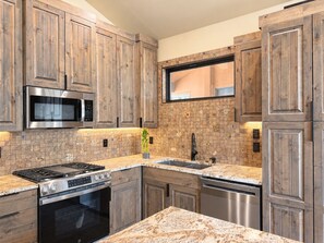 A kitchen with wooden cabinets, a microwave, a stove, a dishwasher, and a tiled backsplash. - Purple Sage Place (Springdale)