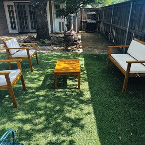 A backyard with a wooden table, two chairs, a grill, and a stone pathway.