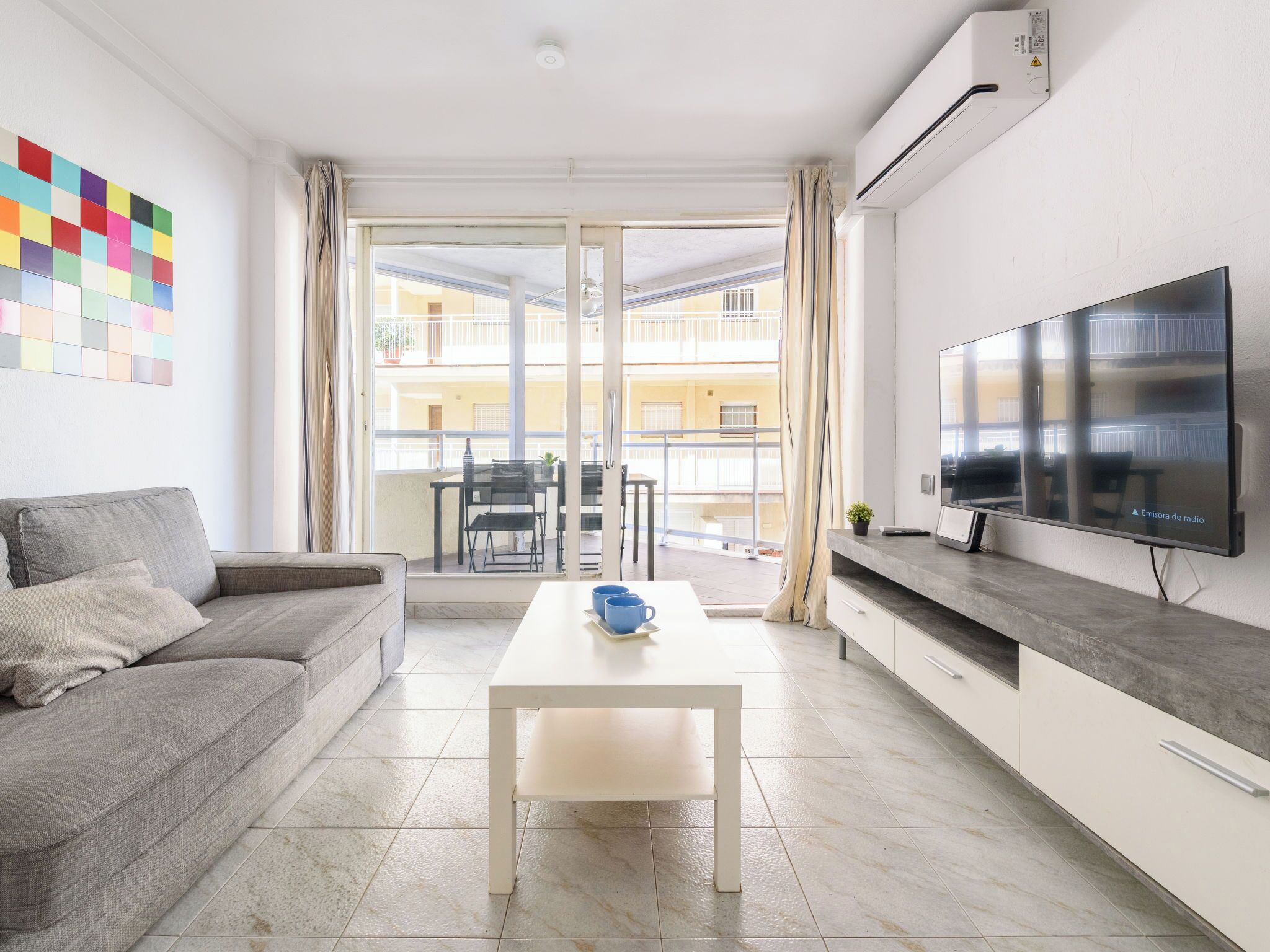 Ein modernes Wohnzimmer mit einer Couch, einem Couchtisch, einem Flachbildfernseher und einem Balkon mit Blick auf ein Gebäude.