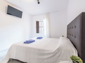 A bedroom with a bed, a television mounted on the wall, a window with curtains, and a potted plant. - Skorpios by Interhome (Salou)