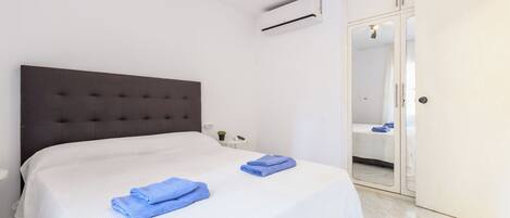 Un dormitorio con una cama grande, una mesita de noche, un equipo de aire acondicionado, un armario y un baño visible a través de una puerta de cristal.