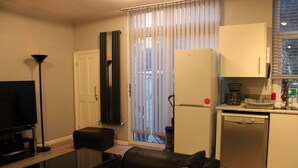 Un ambiente compatto con TV a schermo piatto, divano, macchina del caffè, lavastoviglie e una porta scorrevole in vetro che dà sull'esterno.