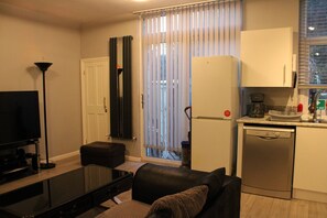 A compact living space with a flat-screen TV, a sofa, a coffee maker, a dishwasher, and a sliding glass door to the outside. - Home Away From Home in Selhurst Park (London)