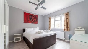 Una camera da letto con un letto, una ventola a soffitto, una finestra con tende, un termosifone e una scrivania.