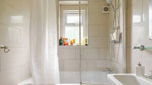 Un bagno con vasca, doccia e finestra, con articoli da toilette sul davanzale.