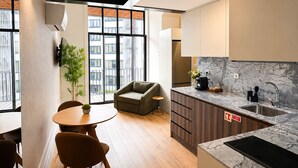 A modern kitchen with a marble countertop, a built-in oven, and a sink. There is a dining area with a round table and chairs, and a sofa. - Passos Collection 263 (Porto)