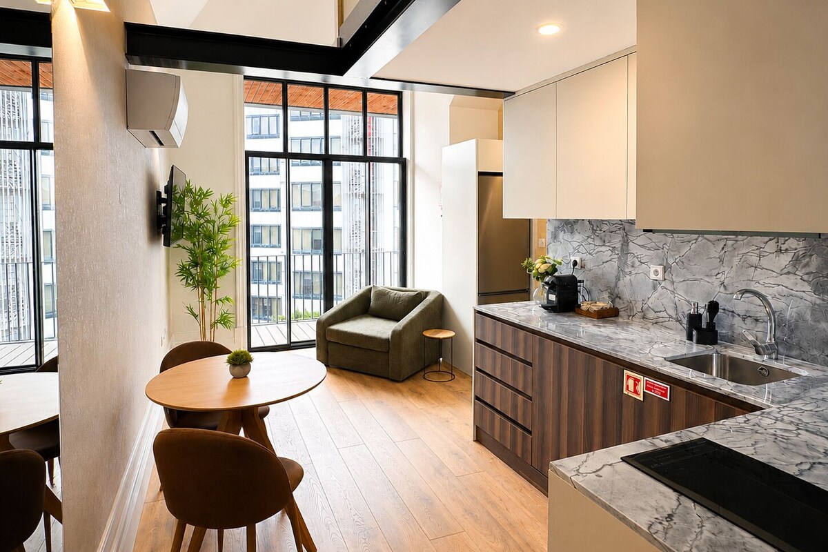 Eine moderne Küche mit Marmorarbeitsplatte, einem Backofen und einem Spülbecken. Es gibt einen Essbereich mit rundem Tisch und Stühlen sowie eine Sitzecke mit einer Couch.