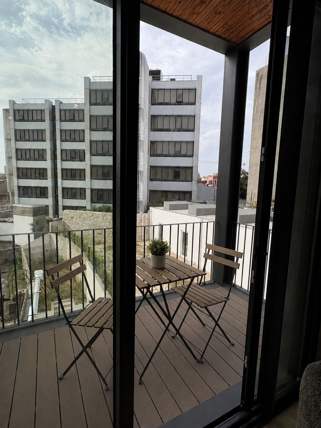 A balcony with a wooden table, two chairs, and a potted plant.