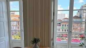 A room with a round wooden table, two chairs, a vase with flowers, and large windows with a city view. - Passos Collection 263 (Porto)
