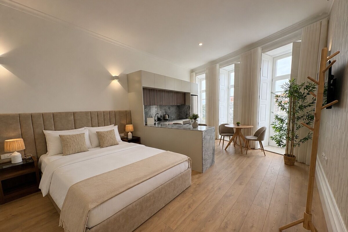 Ein Schlafzimmer mit einem großen Bett, Nachttischen, einem Schreibtisch und einem Stuhl. Es gibt eine kleine Küchenzeile mit Spüle und Schränken.