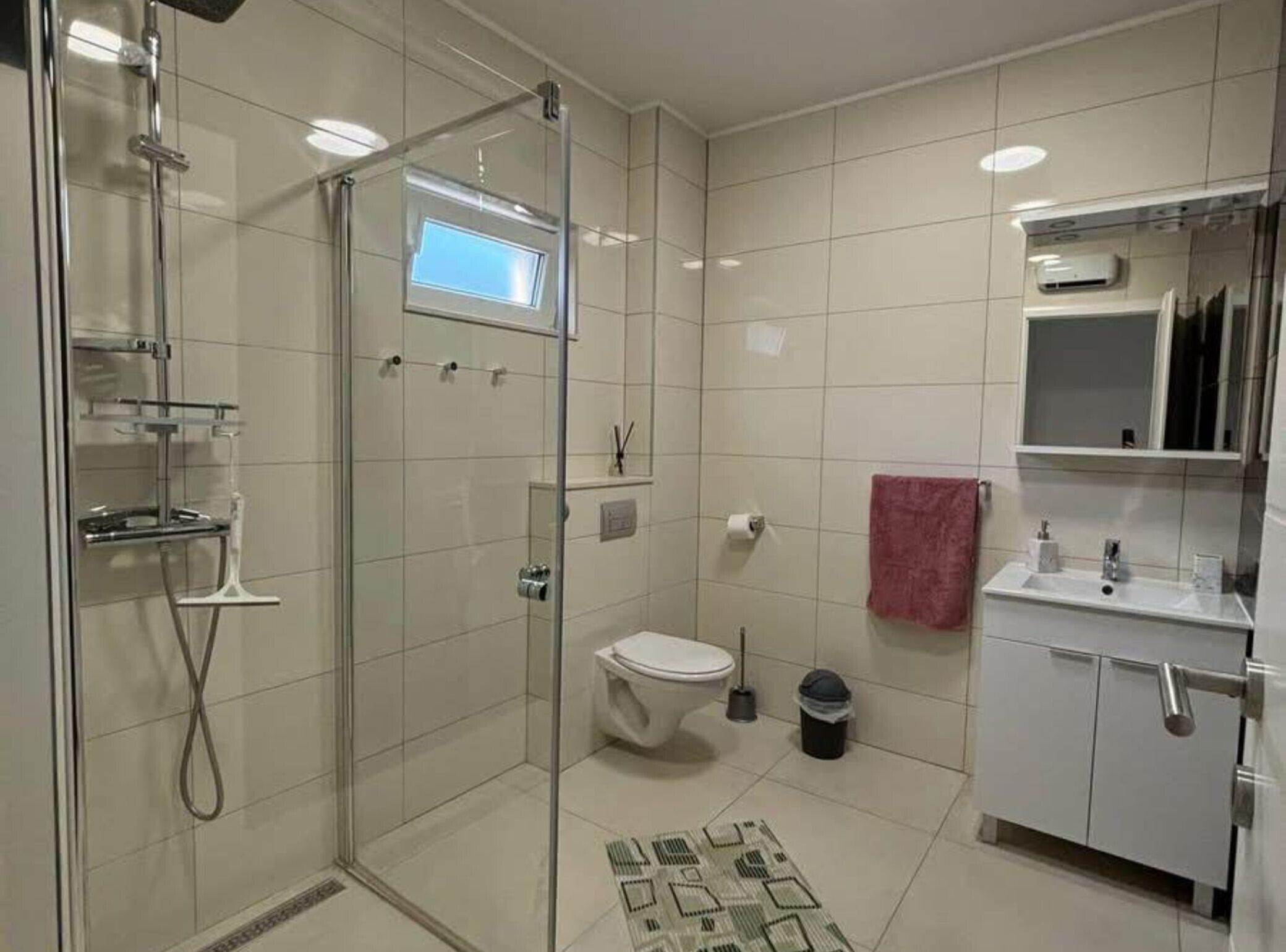 Een moderne badkamer met een douchecabine van glas, een toilet, een wastafel met spiegel en een betegelde vloer.
