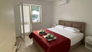 Een hotelkamer met een bed, een raam met zonwering, een deur en een klein nachtkastje.