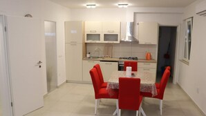 Een compacte keuken met witte kasten, een eettafel met rode stoelen en een betegelde vloer.