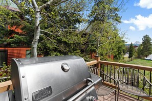 Ein Grill auf einer Terrasse mit Blick auf ein Haus und Bäume.