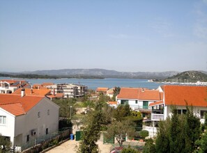 Un área residencial costera con casas de tejados de terracota, un puerto deportivo y una vista despejada del mar y montañas distantes.