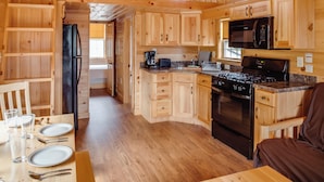A wooden cabin interior with a kitchen, dining area, and a cozy living space.