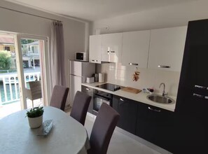 A modern kitchen with white cabinets, a microwave, a sink, and a dining area with chairs and a table. - Two Bedroom Apartment with Balcony and River View (Rogotin)
