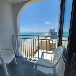 A balcony with white plastic chairs, a view of the beach, and a building in the distance. - Beach Life Honeymoon Suite with Jacuzzi DW1613 (Myrtle Beach)