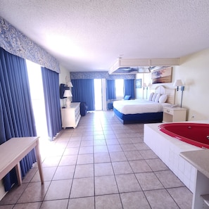 Ein Hotelzimmer mit einem Bett, einer roten Badewanne, einem Schreibtisch, einem Stuhl und einem Fenster mit Vorhängen.