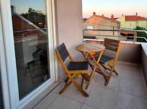 A balcony with a glass door, two wooden chairs, and a small round table. - Two Bedroom Apartment with Sea View and Balcony (Zadar)