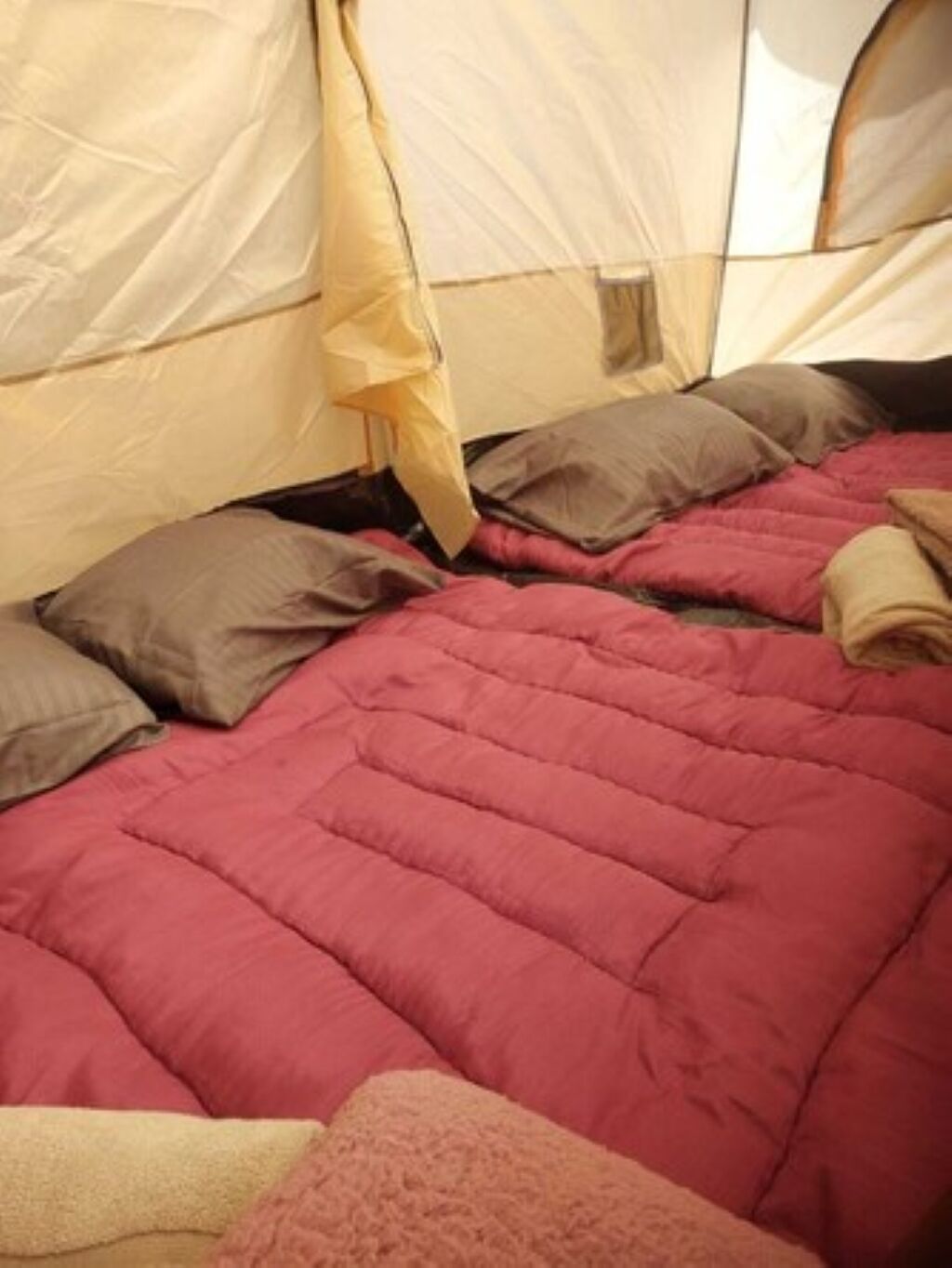 A tent with a bed inside, featuring a red quilt and beige pillows.