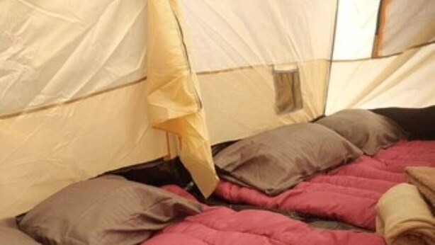 Ein Zelt mit einem Bett im Inneren, ausgestattet mit einer roten Decke und beigen Kissen.
