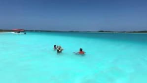 Ein klares, türkisfarbenes Meer mit einem Boot und einer Person im Wasser.