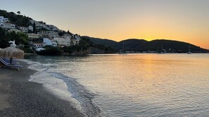 A coastal scene with a beach, a row of sun loungers, and buildings on a hillside. - Family & Friends Studio with balcony / Near to Sea (Poros)