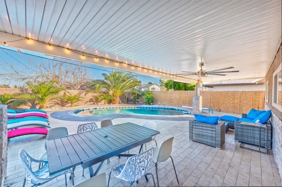 An outdoor pool area with a covered patio, seating, and a table.