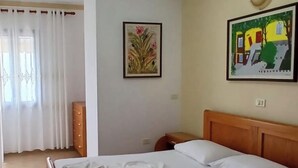 Une chambre d’hôtel avec un lit, un luminaire au plafond, un tableau et une fenêtre avec des rideaux.