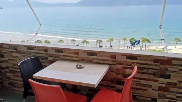 Une terrasse avec une table et des chaises, donnant sur une plage et la mer.