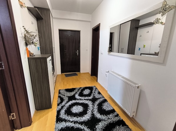 Un couloir avec un tapis à motifs noir et blanc, un radiateur blanc et un miroir accroché au mur.