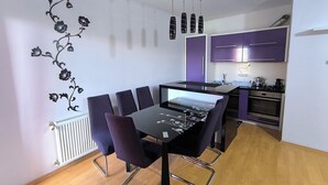 A modern kitchen with purple cabinets, a dining table with chairs, and a radiator on the wall. - Peaceful & Cozy Apartment Gostivar (Gostivar)