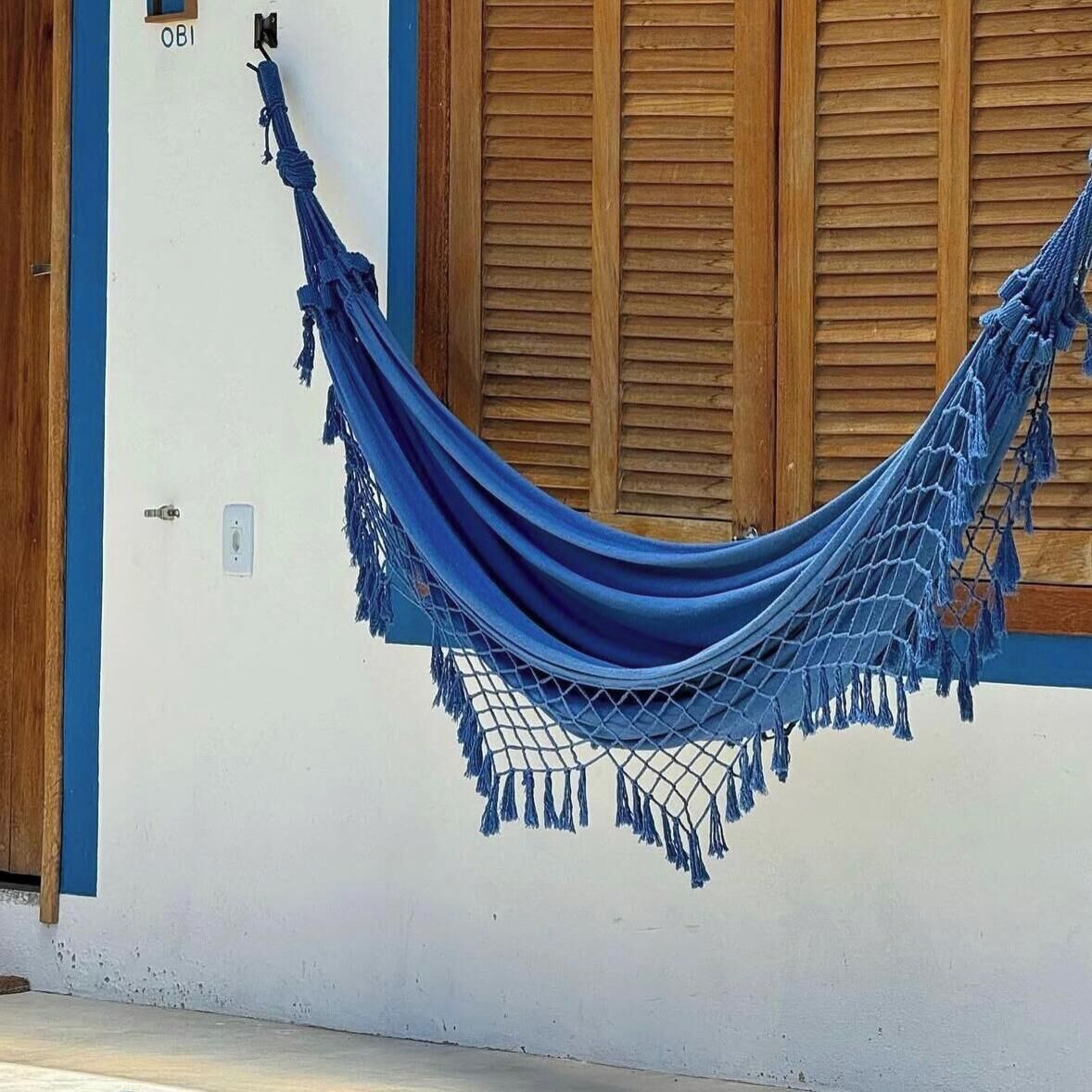 A hammock tied to a wall with wooden shutters, a door with a lock, and a small window.
