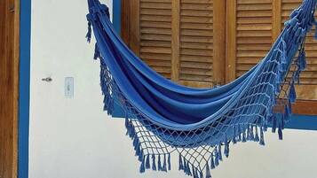 A hammock tied to a wall with wooden shutters, a door with a lock, and a small window.