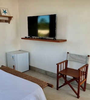 Una habitación con una cama, un refrigerador blanco pequeño, una silla de madera, un televisor montado y una estantería decorada con una estrella.