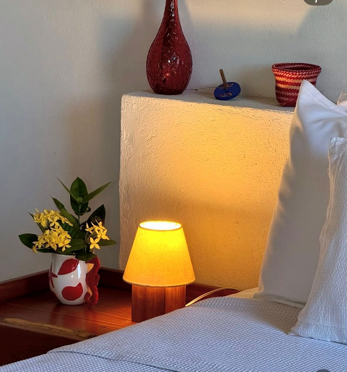 A bedside table with a lamp, a vase with flowers, and a decorative item on a nightstand.