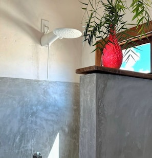 Un baño con ducha, un jarrón rojo y una ventana con vistas.