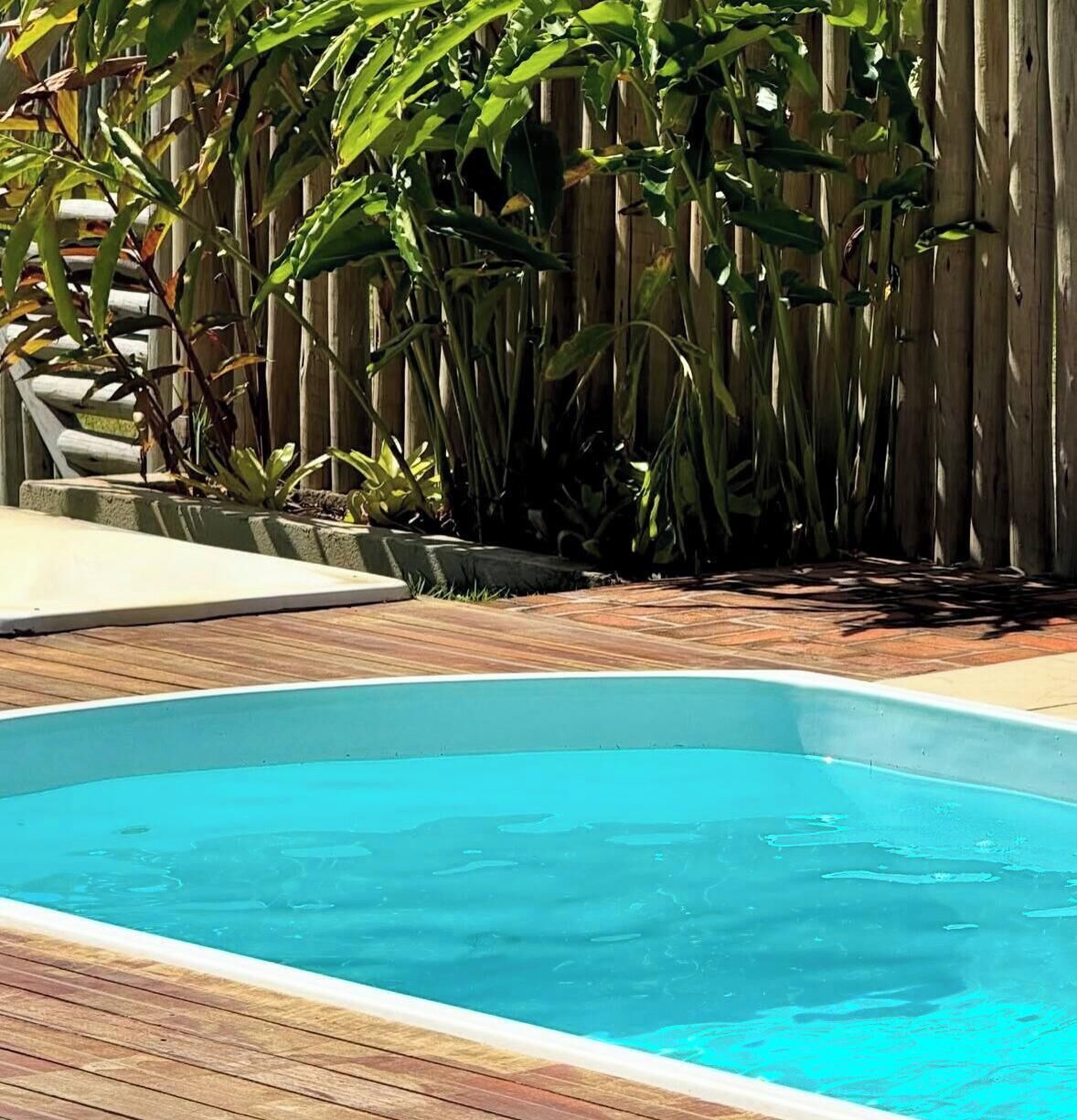 Piscina rectangular con borde de madera, rodeada por una cerca de madera y diversas plantas.