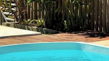Piscina rectangular con borde de madera, rodeada por una cerca de madera y diversas plantas.
